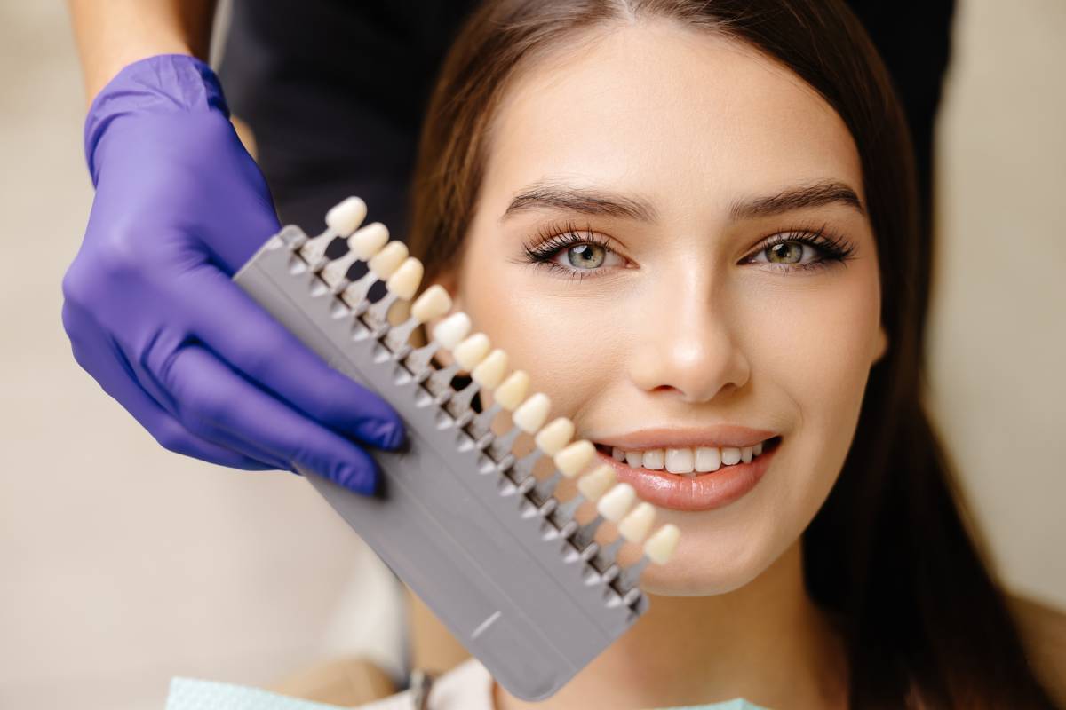 Dentist choosing teeth enamel shade color for young smiling female patient before whitening procedure